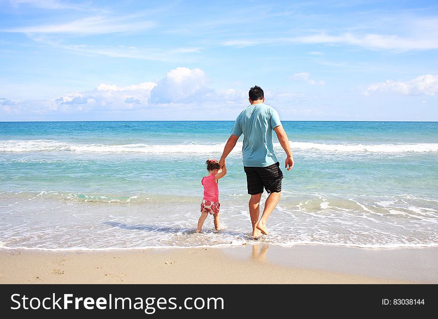 Man and daughter walking in waves on sandy beach on sunny day. Man and daughter walking in waves on sandy beach on sunny day.