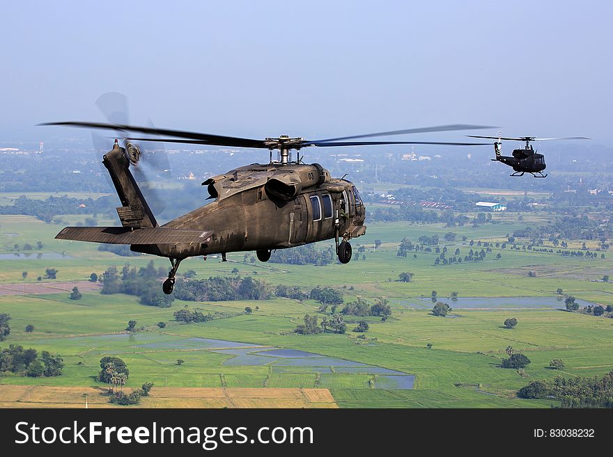 Brown Helicopter Flying Above Green Field During Daytime