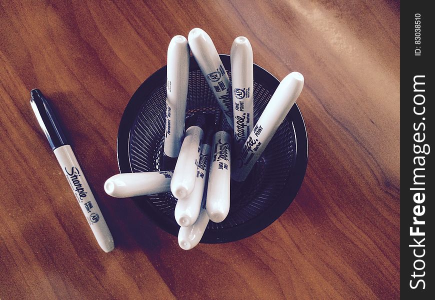 Sharpie black marker pens in cup holder on wooden desk. Sharpie black marker pens in cup holder on wooden desk.