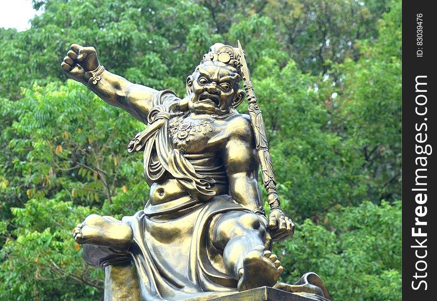Statue of golden warrior in fight pose outdoors among trees. Statue of golden warrior in fight pose outdoors among trees.