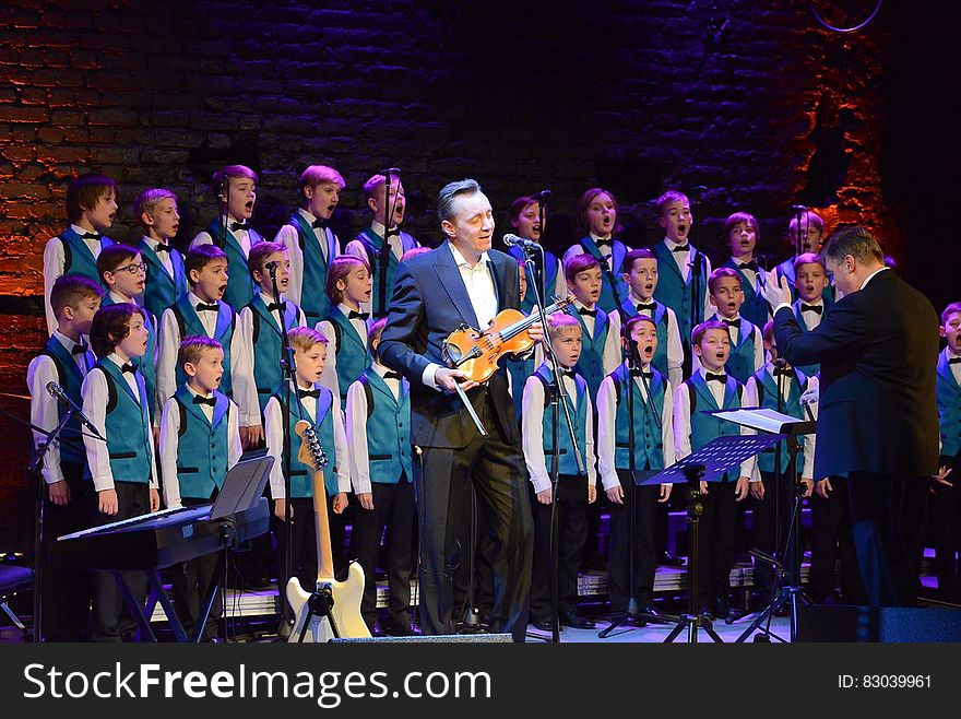 Violinist and children's choir performing onstage with conductor. Violinist and children's choir performing onstage with conductor.