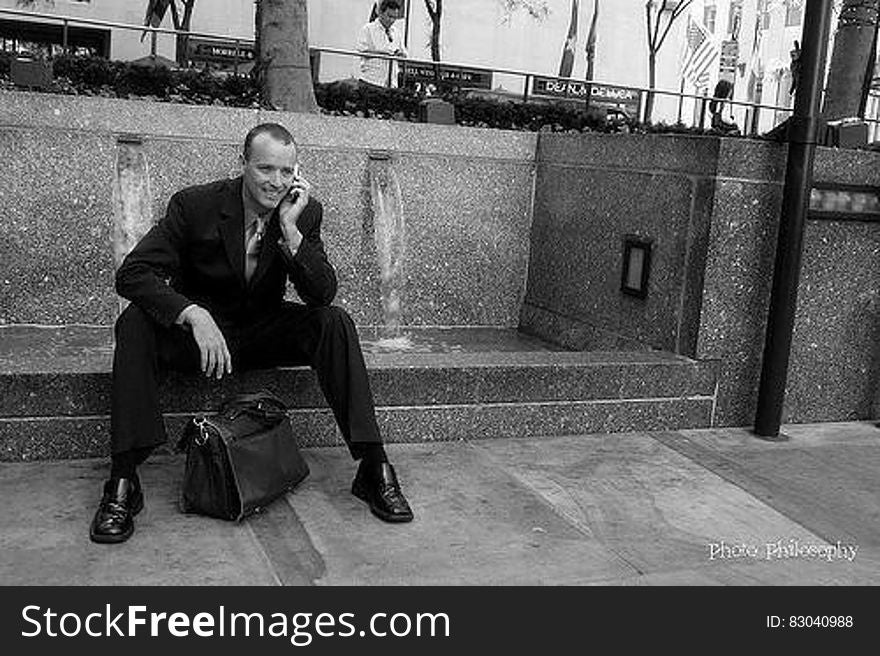 Businessman sitting on sidewalk outside using cellphone in black and white. Businessman sitting on sidewalk outside using cellphone in black and white.