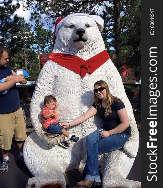 Family posing in front of white polar bear statue with red scarf and Christmas Santa hat on sunny day. Family posing in front of white polar bear statue with red scarf and Christmas Santa hat on sunny day.