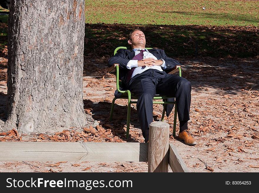 Businessman sitting in lawn chair under tree in sunshine. Businessman sitting in lawn chair under tree in sunshine.