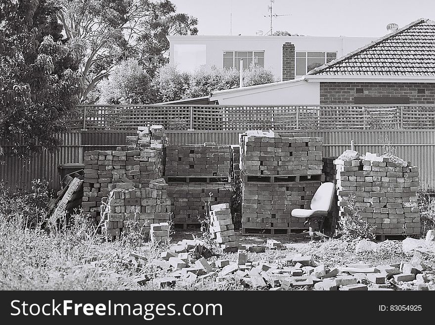 Bricks piled against fencing in backyard in black and white. Bricks piled against fencing in backyard in black and white.