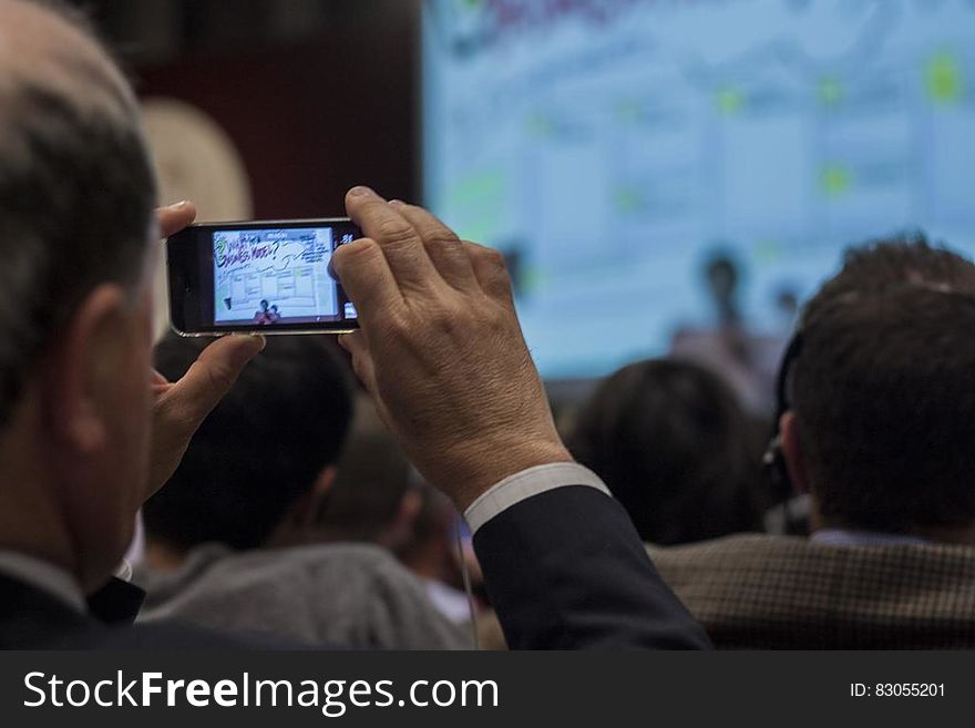 Man in business suit recording event from audience using smartphone. Man in business suit recording event from audience using smartphone.