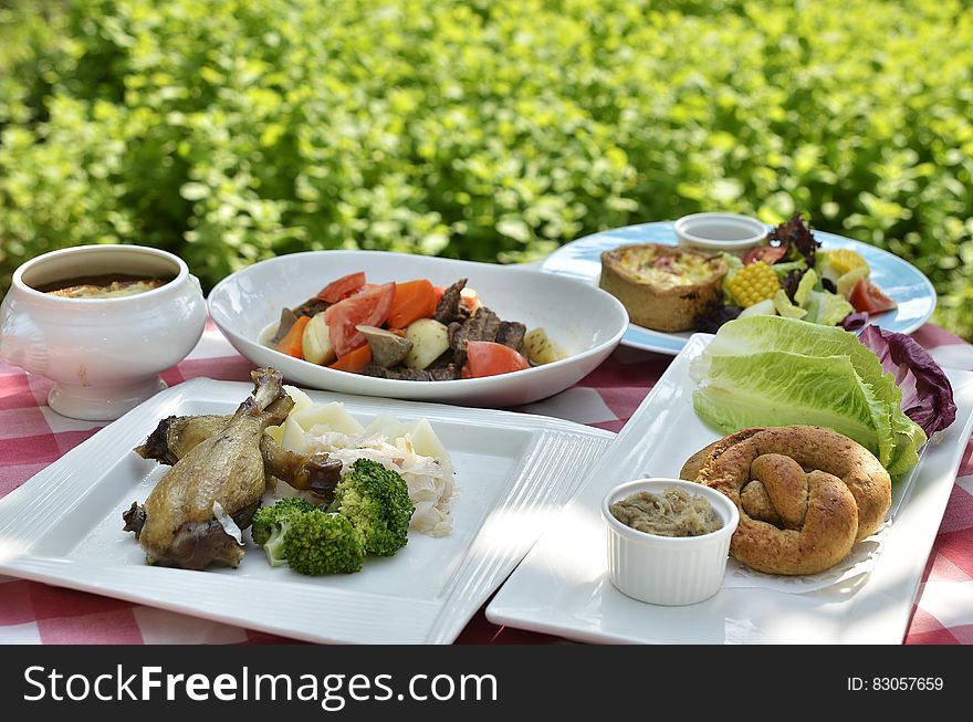 White china plates with food on table in sunny garden next to green bush. White china plates with food on table in sunny garden next to green bush.