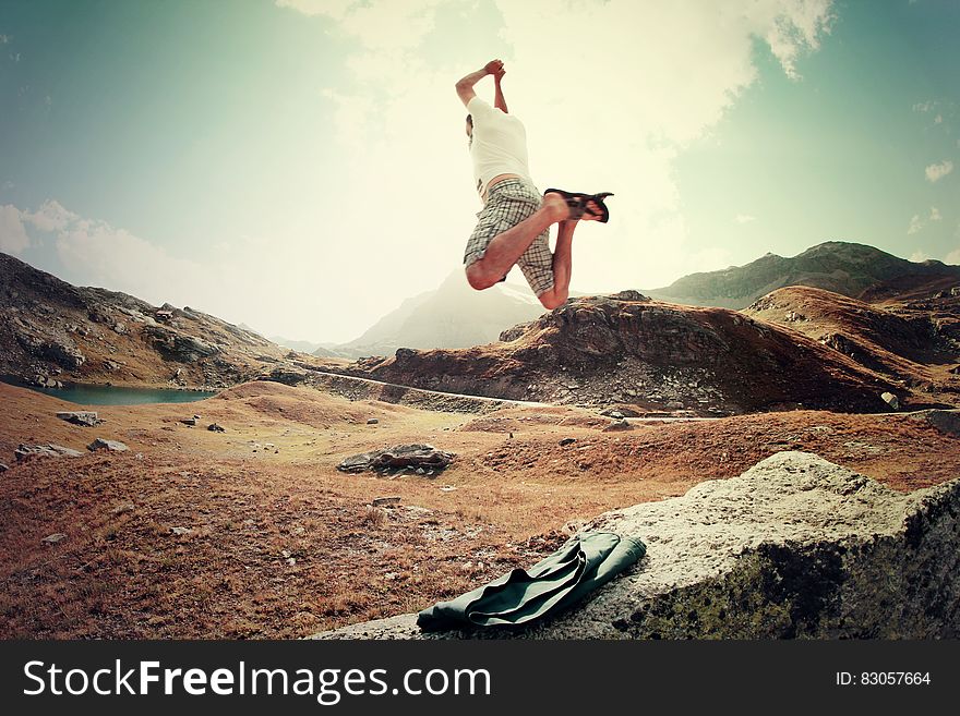 Man jumping in mountains along alpine lake on sunny day.