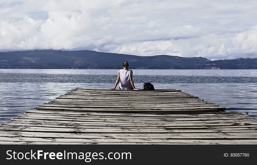 Person Sitting on Brown Wooden Dock Under Cloudy Blue Sky