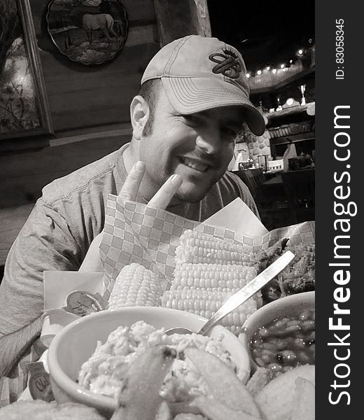 Man in ball cap smiling and gesturing white eating at restaurant in black and white. Man in ball cap smiling and gesturing white eating at restaurant in black and white.