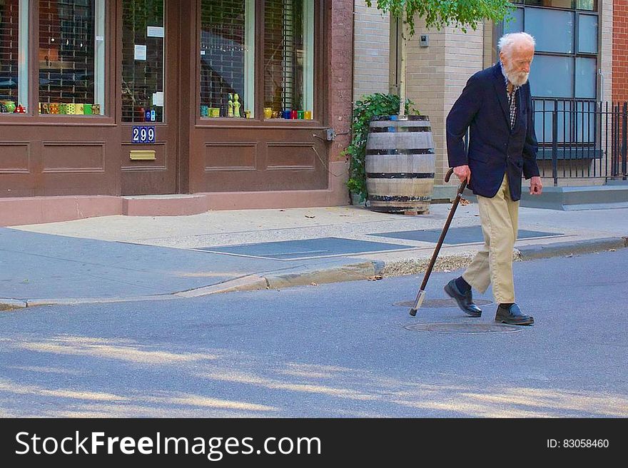 Senior man with walking stick crossing street road.