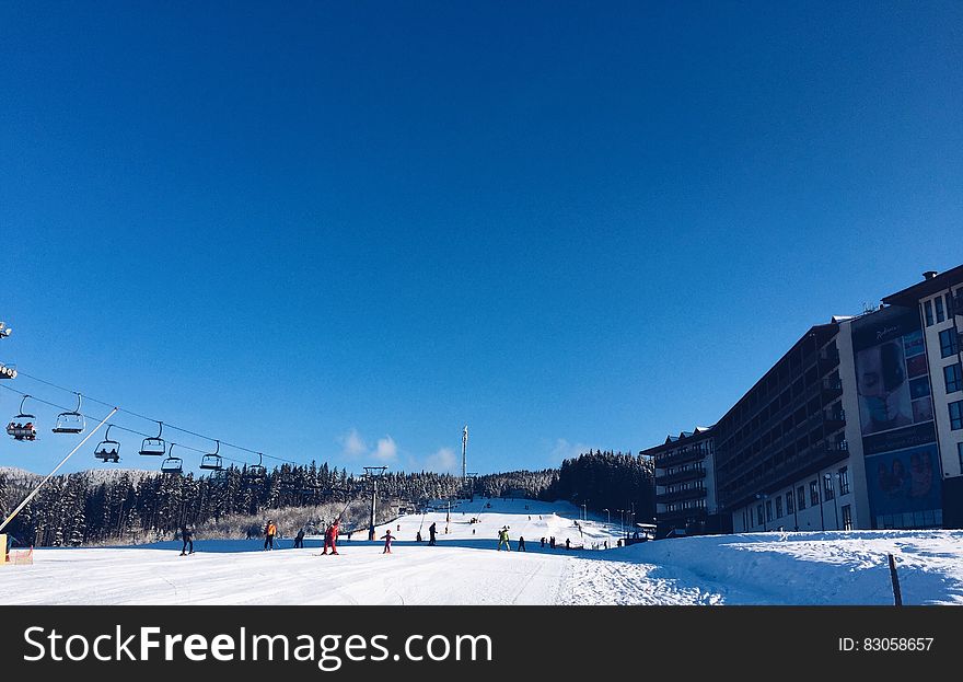 People on a Snowy Ski Hill With a Lift on the Left and a Hotel on the Right