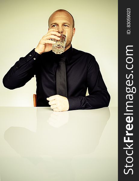 Man in Black Dress Shirt Sitting in Front of White Table Drinking Water