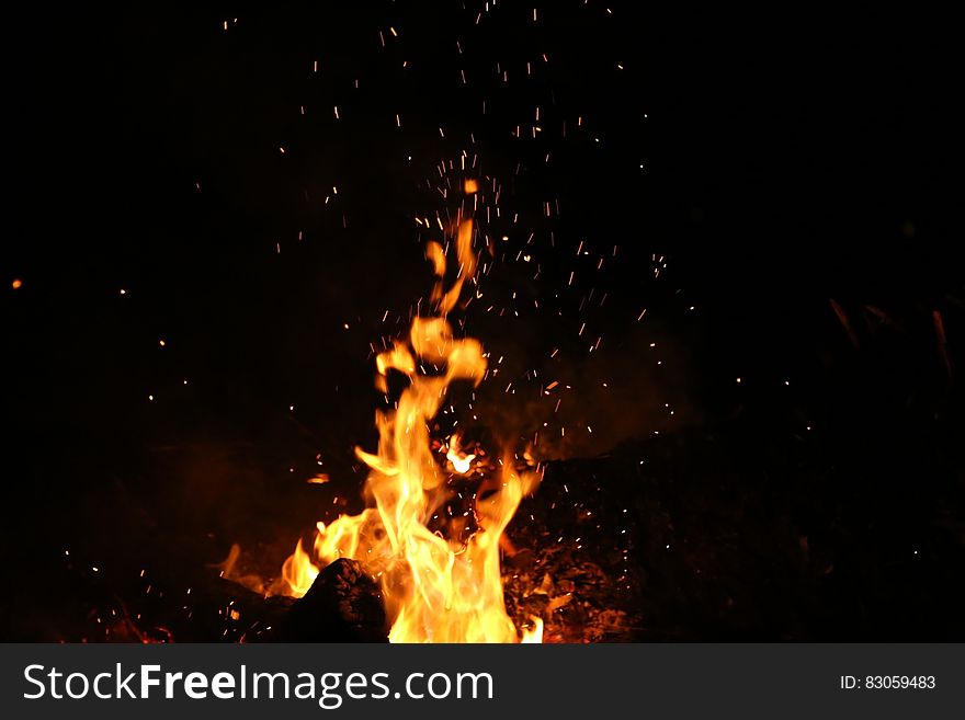 A burning bonfire with yellow flames and hot burning embers rising against a black sky. A burning bonfire with yellow flames and hot burning embers rising against a black sky.