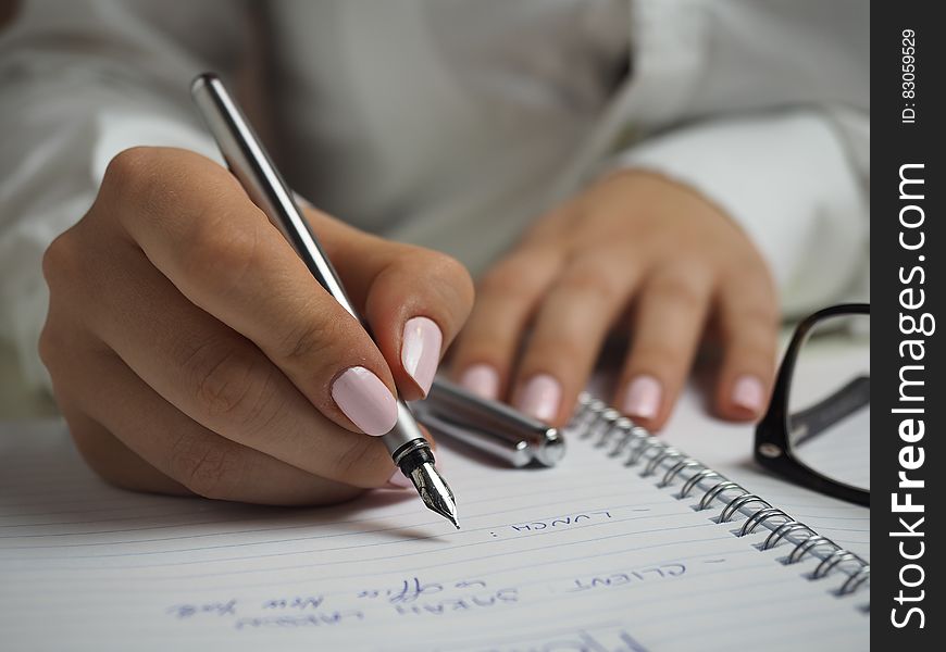 Woman in White Long Sleeved Shirt Holding a Pen Writing on a Paper