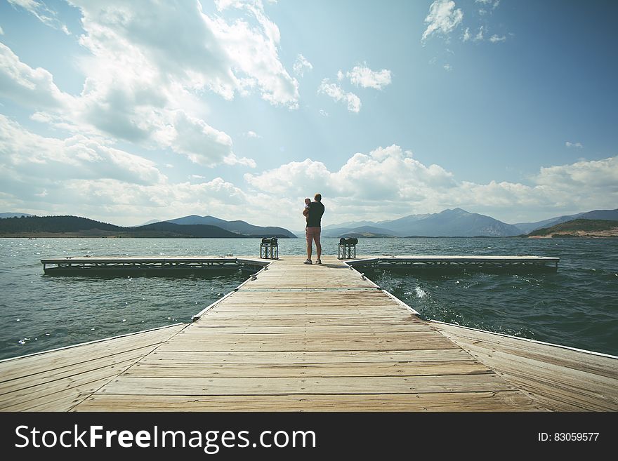 Person Standing on Brown Wooden Dock Under Clue Sky during Daytime