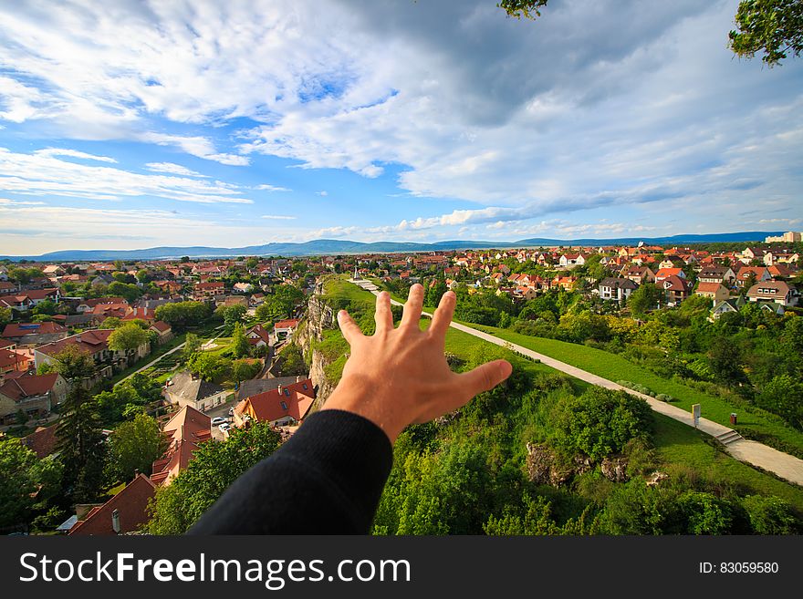 Human Hand Under White and Blue Sky on Green Grass Field