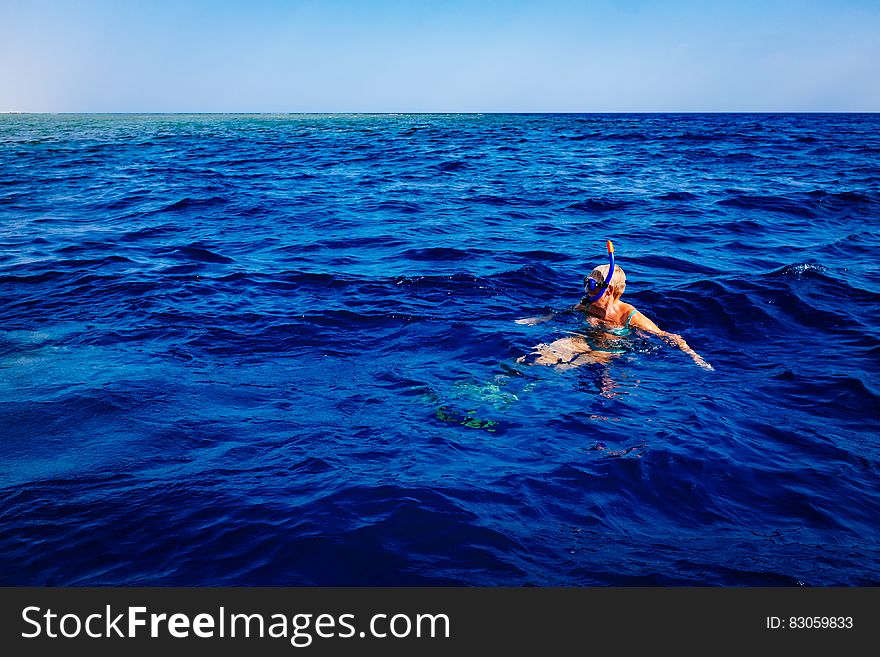 Snorkeler in blue waters with mask and breathing tube on sunny day.