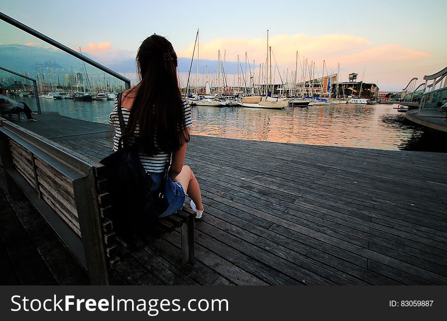 Woman in Black and White Stripe Scoop Neck Shirt Sitting on Brown Wooden Bench in Ship Dock during Daytime