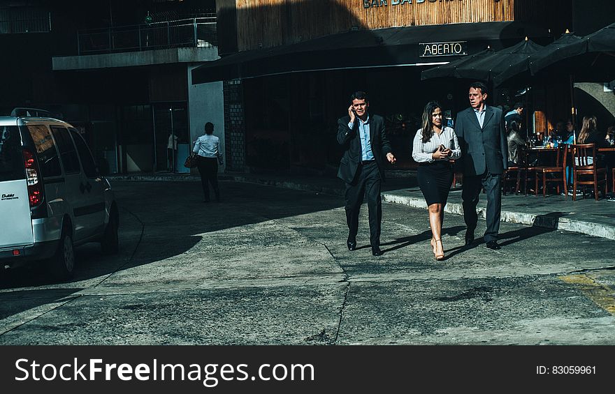 Woman in White Dress Shirt Between Men in Suit Standing on Concrete Ground