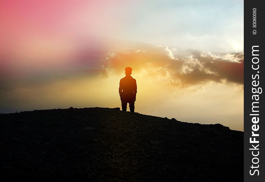 A silhouette of a man standing on a hilltop at sunset. A silhouette of a man standing on a hilltop at sunset.