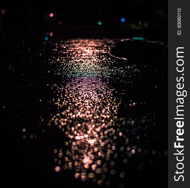 Bokeh lights reflecting on wet pavement at night.