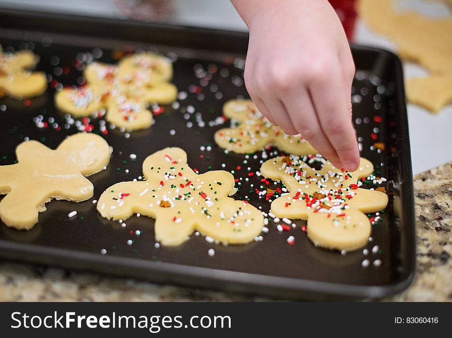 Hand sprinkling colorful nonpareils on gingerbread man cookies on baking tray. Hand sprinkling colorful nonpareils on gingerbread man cookies on baking tray.