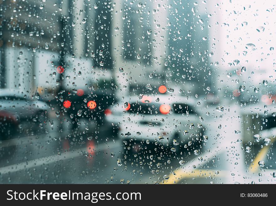 Traffic on rainy streets through water drops on window.