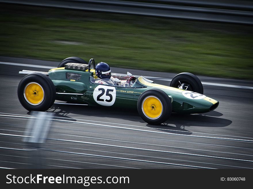 Formula 0ne green racing car numbered 25 traveling at speed on race circuit with white lane markings and green grassy background. Formula 0ne green racing car numbered 25 traveling at speed on race circuit with white lane markings and green grassy background.