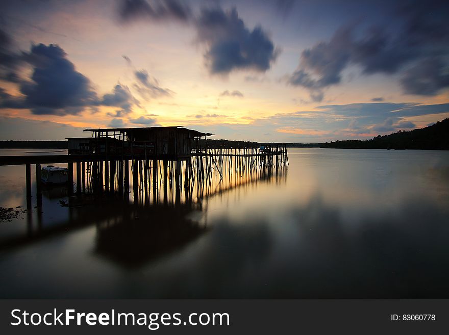 Silhouette Of Wooden House And Walkbridge On Water