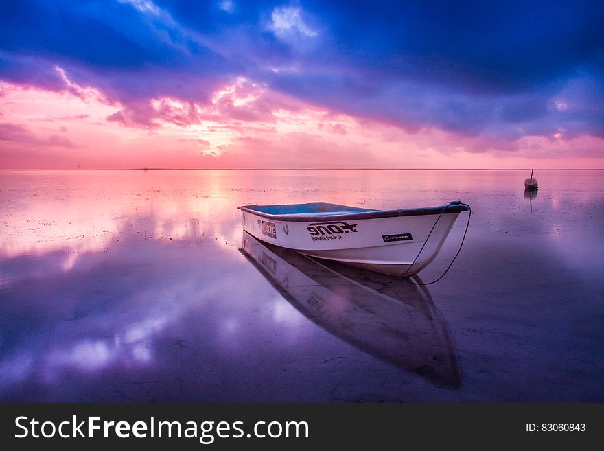 Wooden boat in clear waters reflecting clouds and colors at sunset. Wooden boat in clear waters reflecting clouds and colors at sunset.
