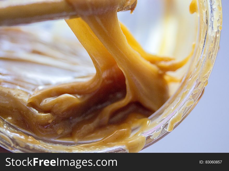 Close up of caramel on wooden spoon inside glass jar. Close up of caramel on wooden spoon inside glass jar.