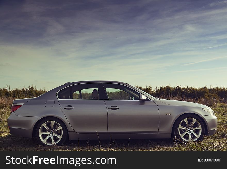 Silver Sedan Parked Far From Green Trees Under Blue Sky During Daytime