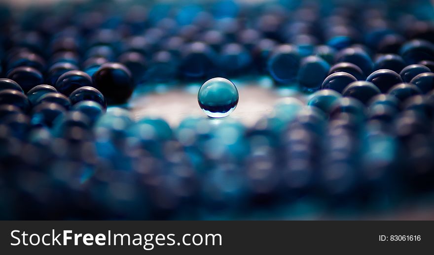 This picture shows a large number of blue opaque glass marbles. In the middle there is a round free space around a single marble located exactly in the center of the picture. This picture shows a large number of blue opaque glass marbles. In the middle there is a round free space around a single marble located exactly in the center of the picture.