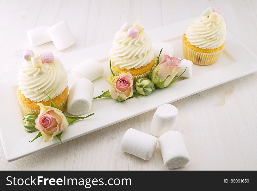 Marshmallows next to tray of frosted cupcakes with rose buds. Marshmallows next to tray of frosted cupcakes with rose buds.