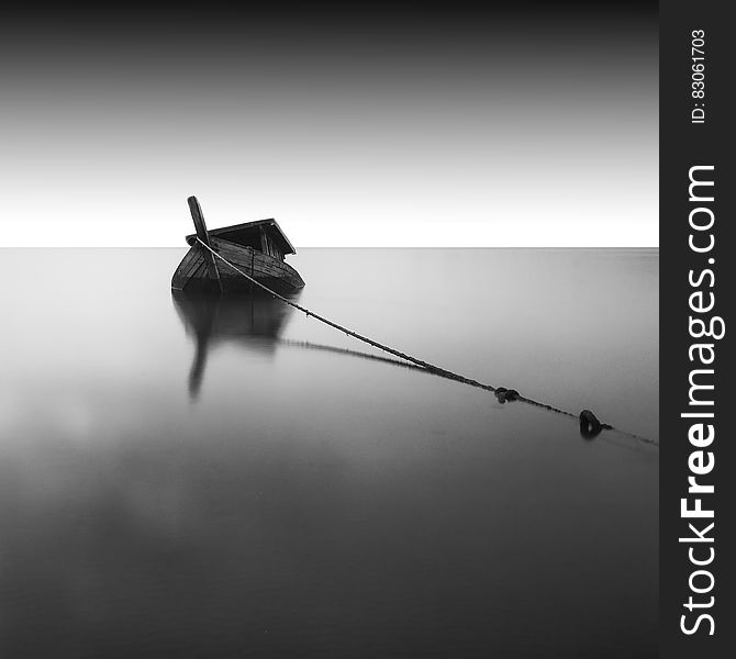 A black and white photo of an anchored wooden boat on still sea surface. A black and white photo of an anchored wooden boat on still sea surface.