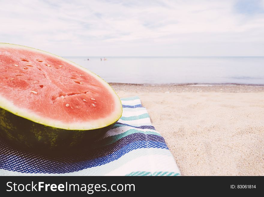 Slice of watermelon on beach blanket on sandy shores.