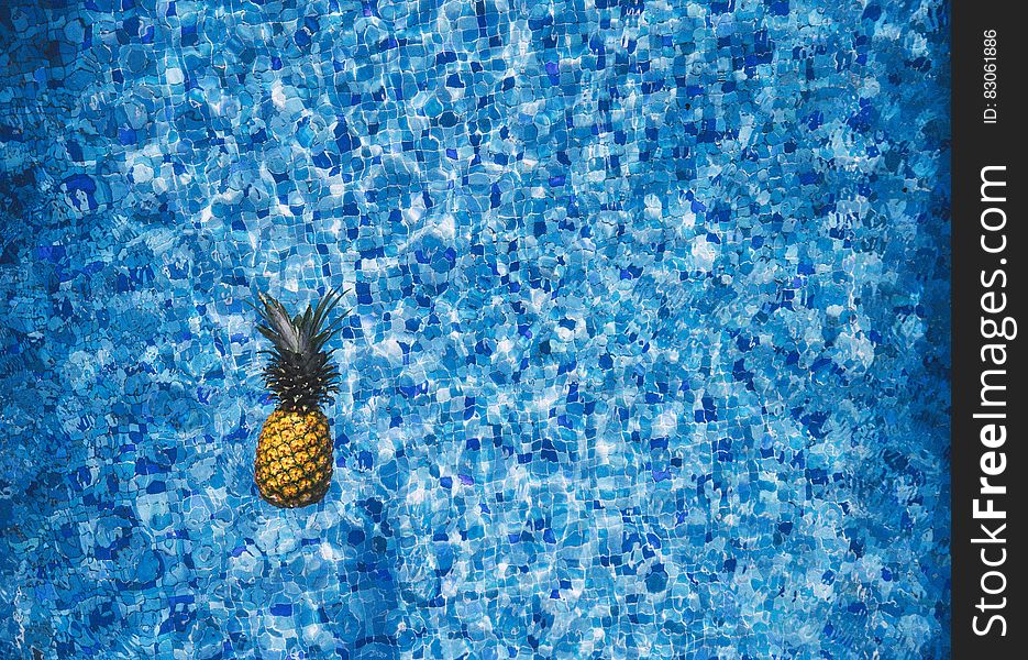 Fresh whole pineapple floating in swimming pool with blue tiles. Fresh whole pineapple floating in swimming pool with blue tiles.