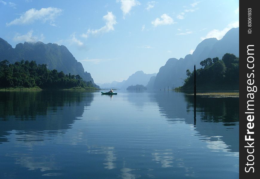 Kayak on blue waters reflecting mountain landscape on sunny day.