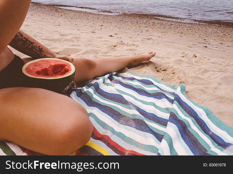 A woman eating a watermelon white sitting on the beach. A woman eating a watermelon white sitting on the beach.