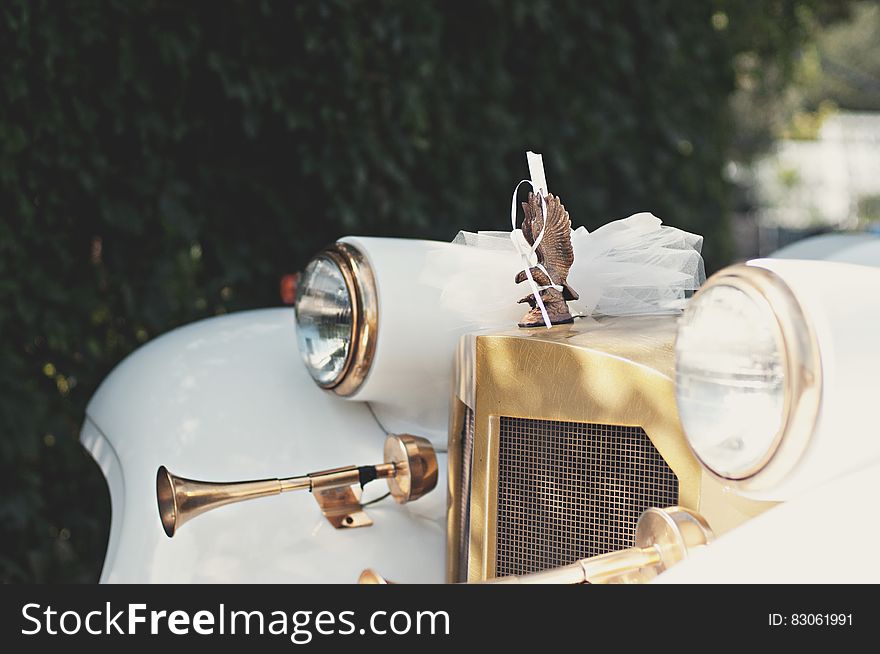 Headlights and hood ornament on front of white vintage car outdoors on sunny day. Headlights and hood ornament on front of white vintage car outdoors on sunny day.