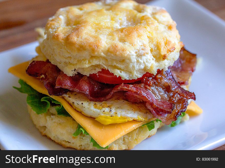 Close up of biscuit sandwich with bacon, egg, cheese and lettuce on white plate. Close up of biscuit sandwich with bacon, egg, cheese and lettuce on white plate.