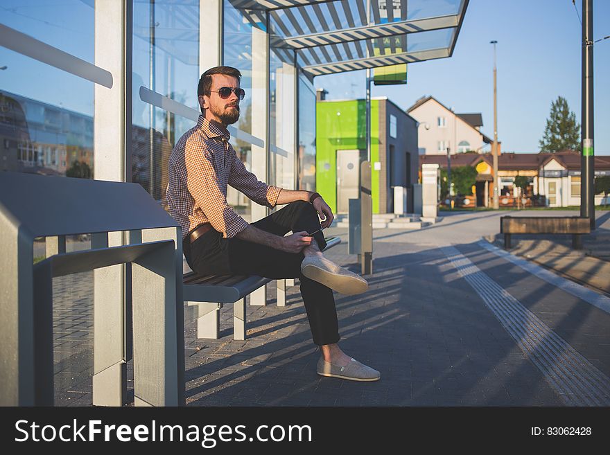 Man Wearing Sunglasses Sitting at Bus Stop during Daytime