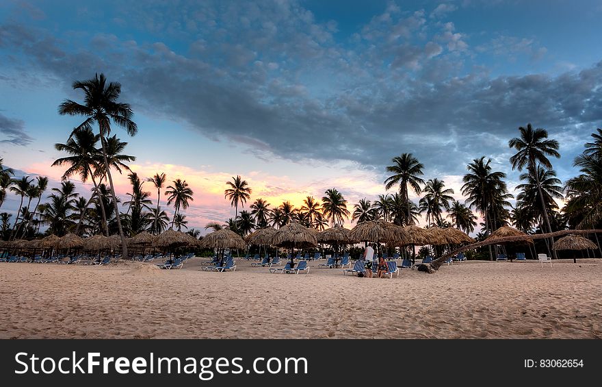 Nipa Hat Surrounded With Palm Trees Under White Clouds And Blue Skies Under Orange Sunset