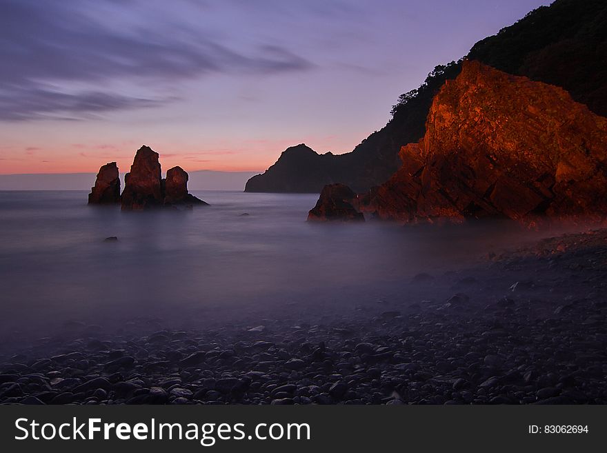 Tall Rock Formation Submerged In Water Near The Shore During Golden Hour