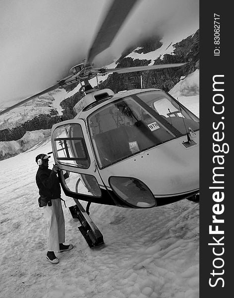 Man standing next to helicopter on snow in mountains in black and white. Man standing next to helicopter on snow in mountains in black and white.