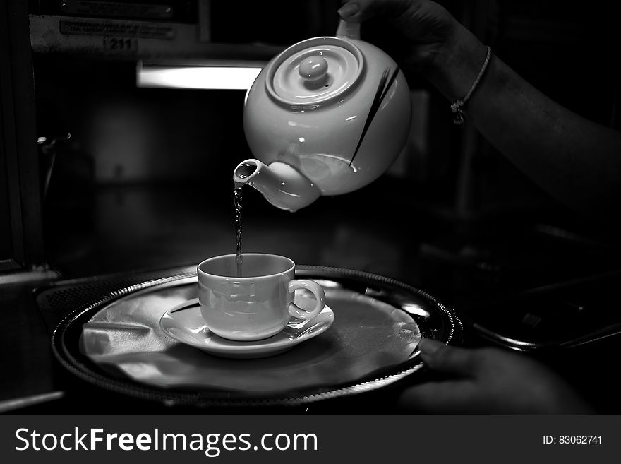 Tea pouring from china pot into cup on saucer and tray in black and white. Tea pouring from china pot into cup on saucer and tray in black and white.