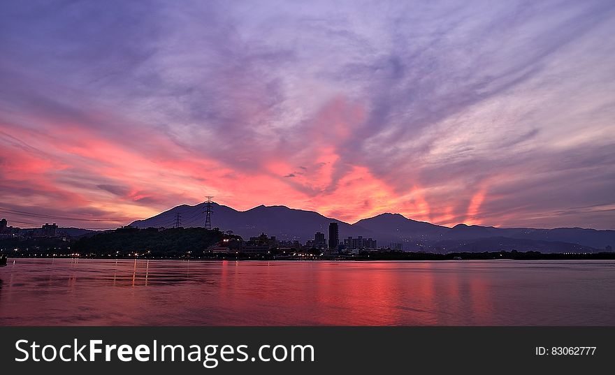 Silhouette Photo of City Buildings Near Sea With Mountain during Golden Time