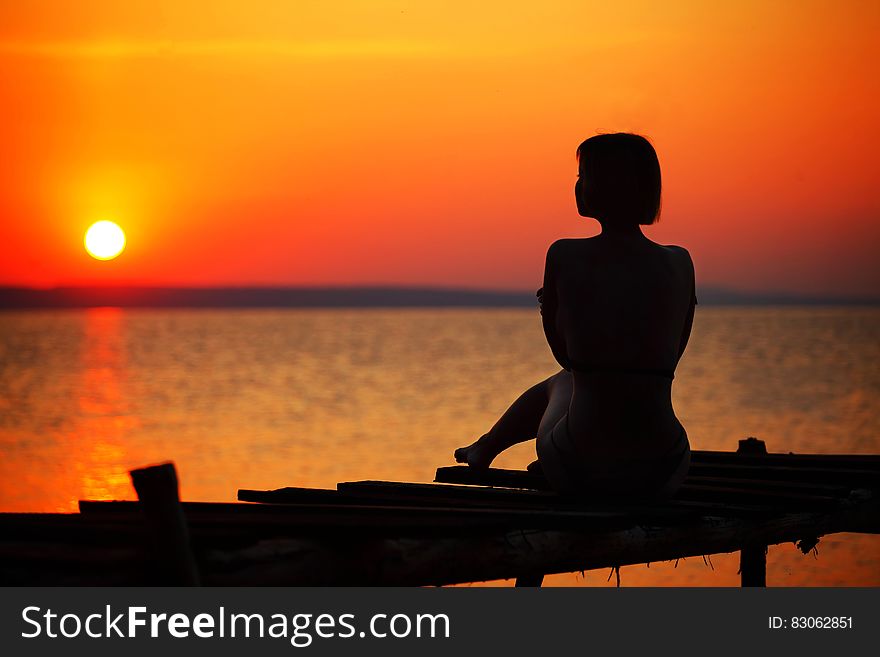 Silhouette Of Woman Sitting On Dock During Sunset