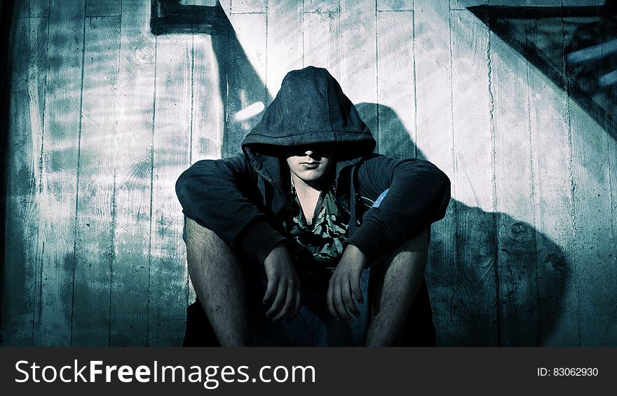 Person Wearing Black Zip Hoodie Sitting in Front of Gray Wooden Plank Wall during Nighttime